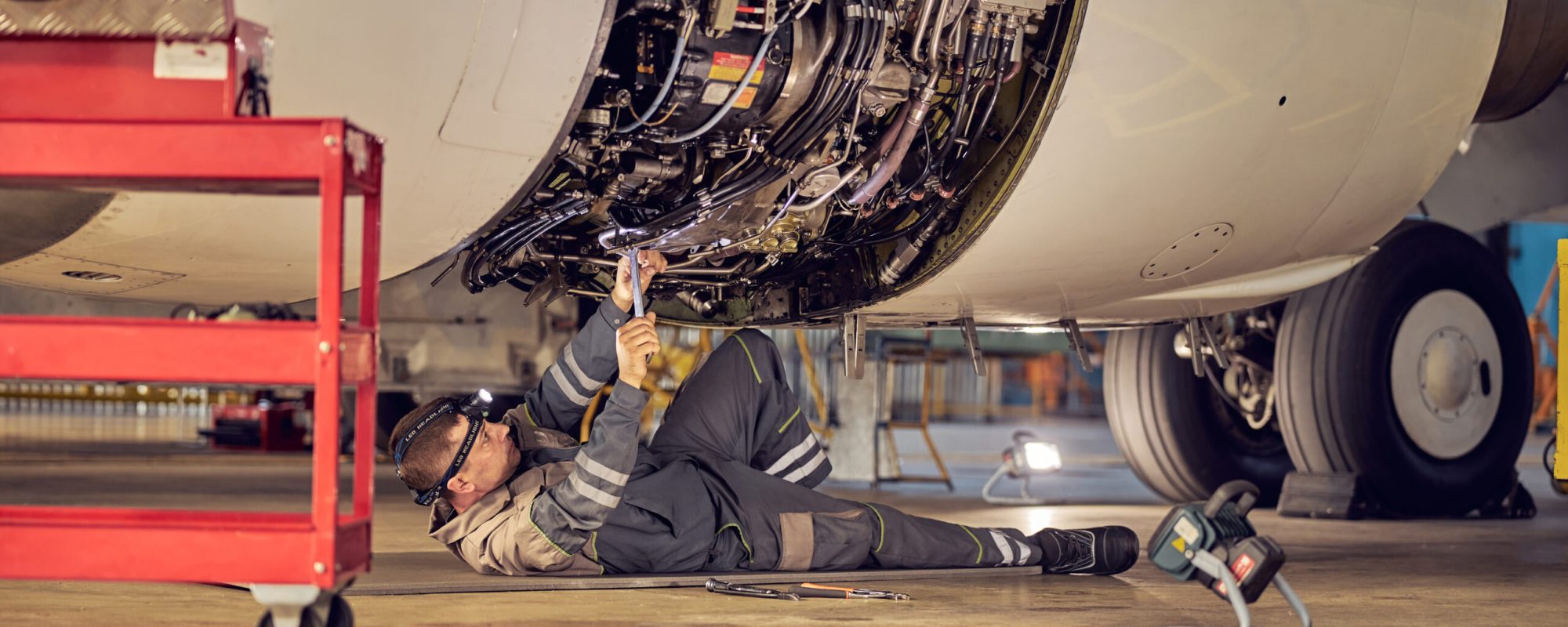 Side view portrait of airplane maintenance mechanic inspecting and tuning plane engine in a hangar